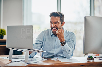 Buy stock photo Shot of a handsome young businessman doing a fist pump while working on a laptop in an office