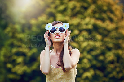 Buy stock photo Portrait of an attractive young woman wearing sunglasses while holding them and standing outside in nature during the day