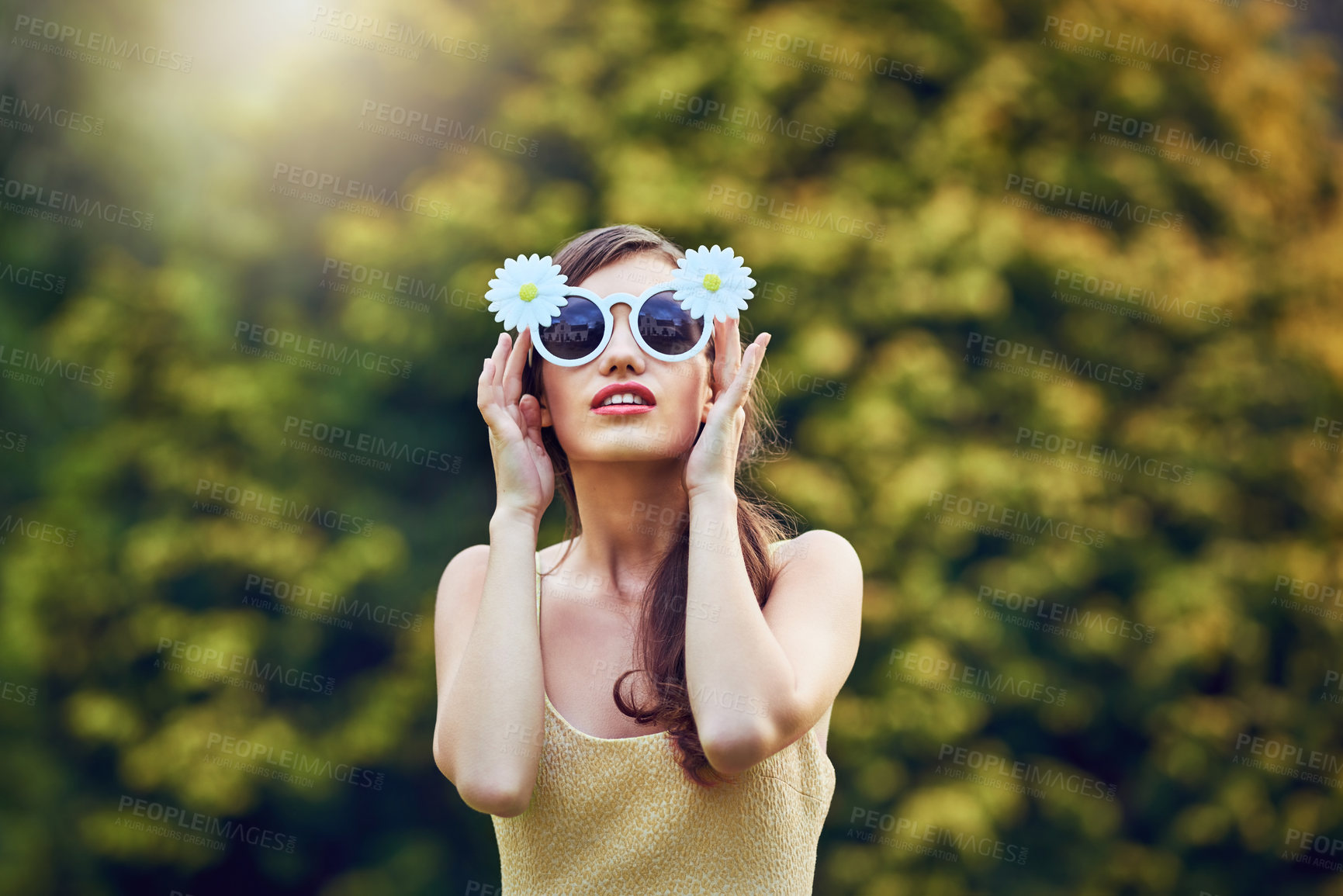 Buy stock photo Portrait of an attractive young woman wearing sunglasses while holding them and standing outside in nature during the day