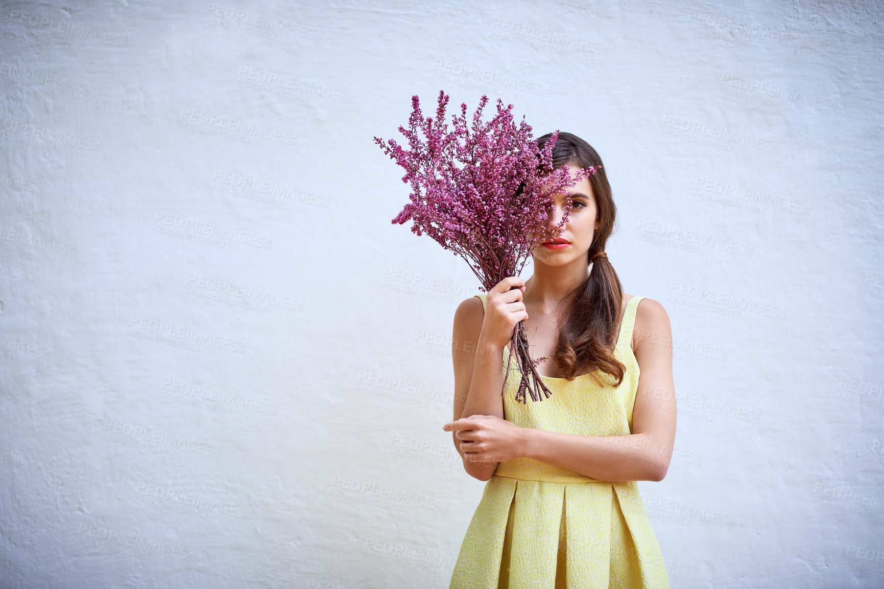 Buy stock photo Studio portrait of a confident young woman hiding behind a bouquet of flowers while standing against a grey background