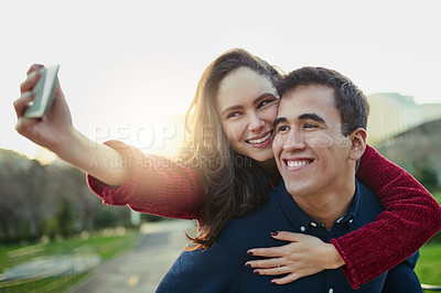Buy stock photo Shot of a young couple taking selfies while enjoying a piggyback ride outdoors
