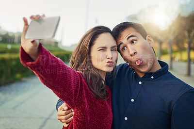 Buy stock photo Shot of a young couple making funny faces while taking a selfie outdoors