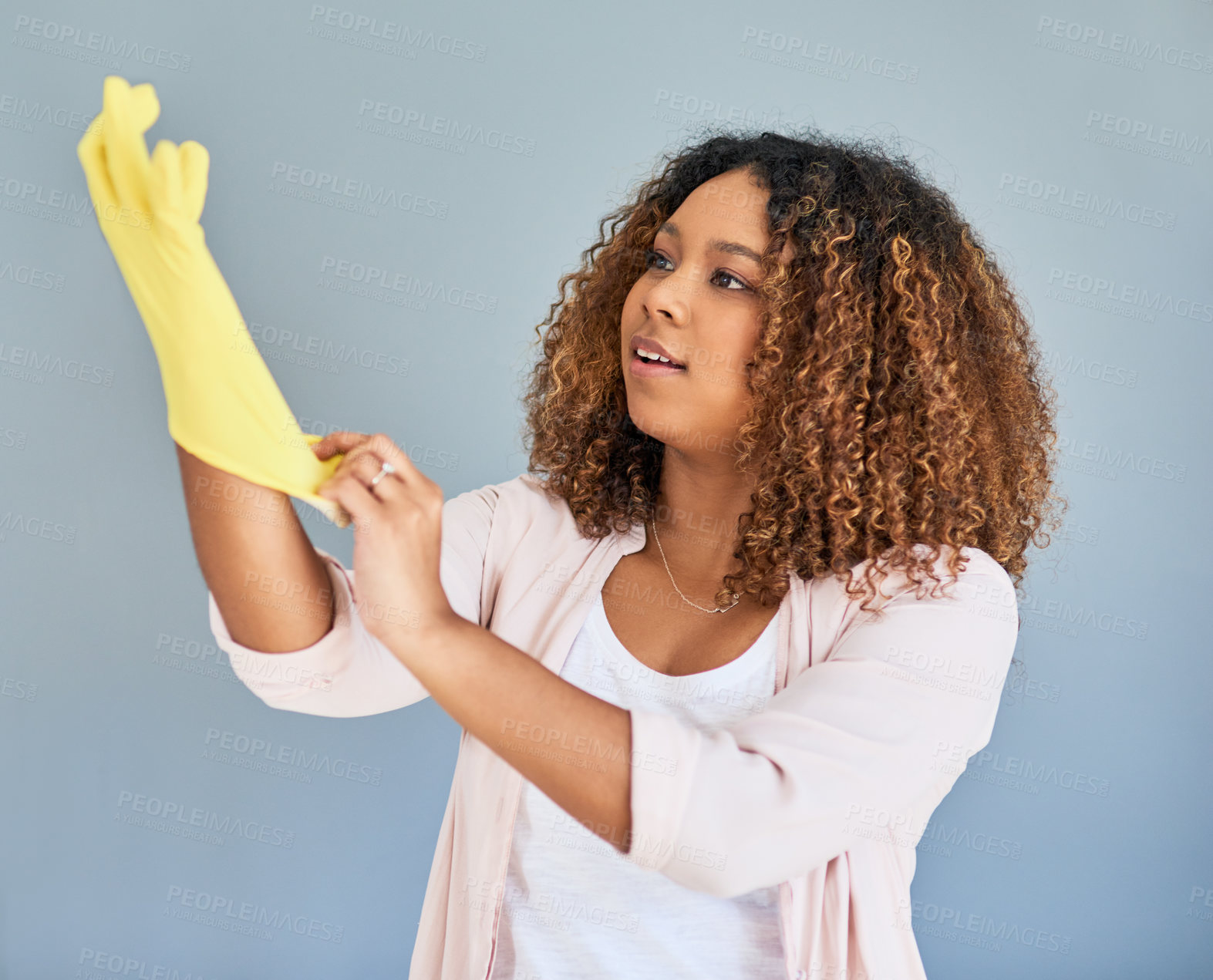 Buy stock photo Studio shot of a young attractive woman putting on rubber gloves against a gray background