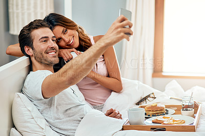 Buy stock photo Shot of a happy young couple taking a selfie while enjoying breakfast in bed together at home
