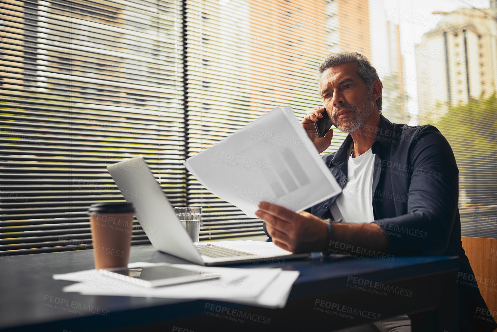 Buy stock photo Businessman, documents and laptop with phone call at cafe for business discussion, conversation or finance. Mature man, employee or accountant talking on mobile smartphone with company statistics