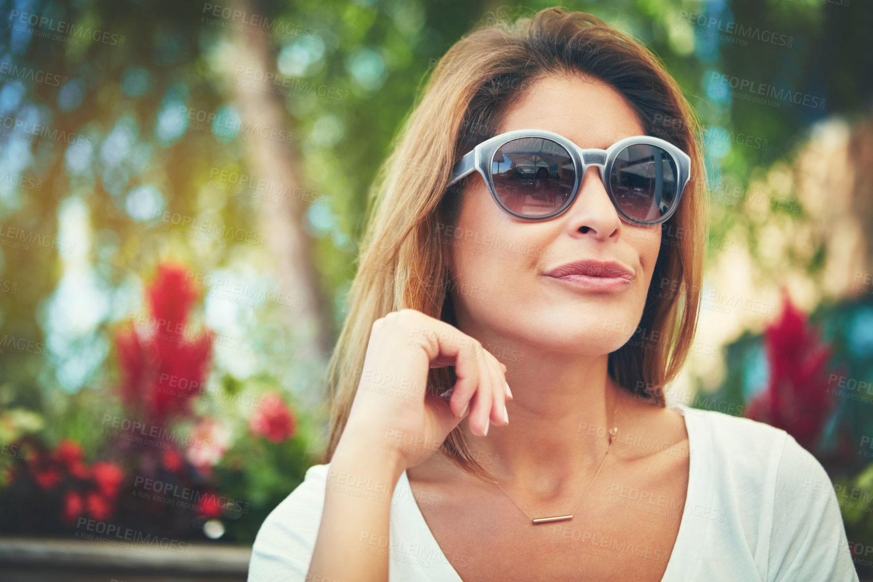Buy stock photo Shot of a confident young woman wearing sunglasses while sitting at a restaurant outside during the day