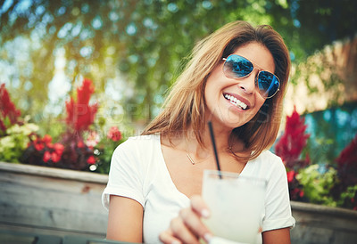 Buy stock photo Shot of a cheerful young woman wearing sunglasses and enjoying a cold beverage while being seated at a restaurant outside during the day