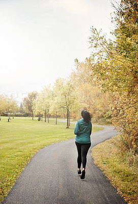 Buy stock photo Rearview shot of a young woman going for a run in nature