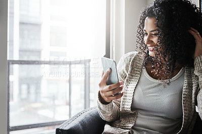 Buy stock photo Shot of a cheerful young woman relaxing while texting on her cellphone at home during the day