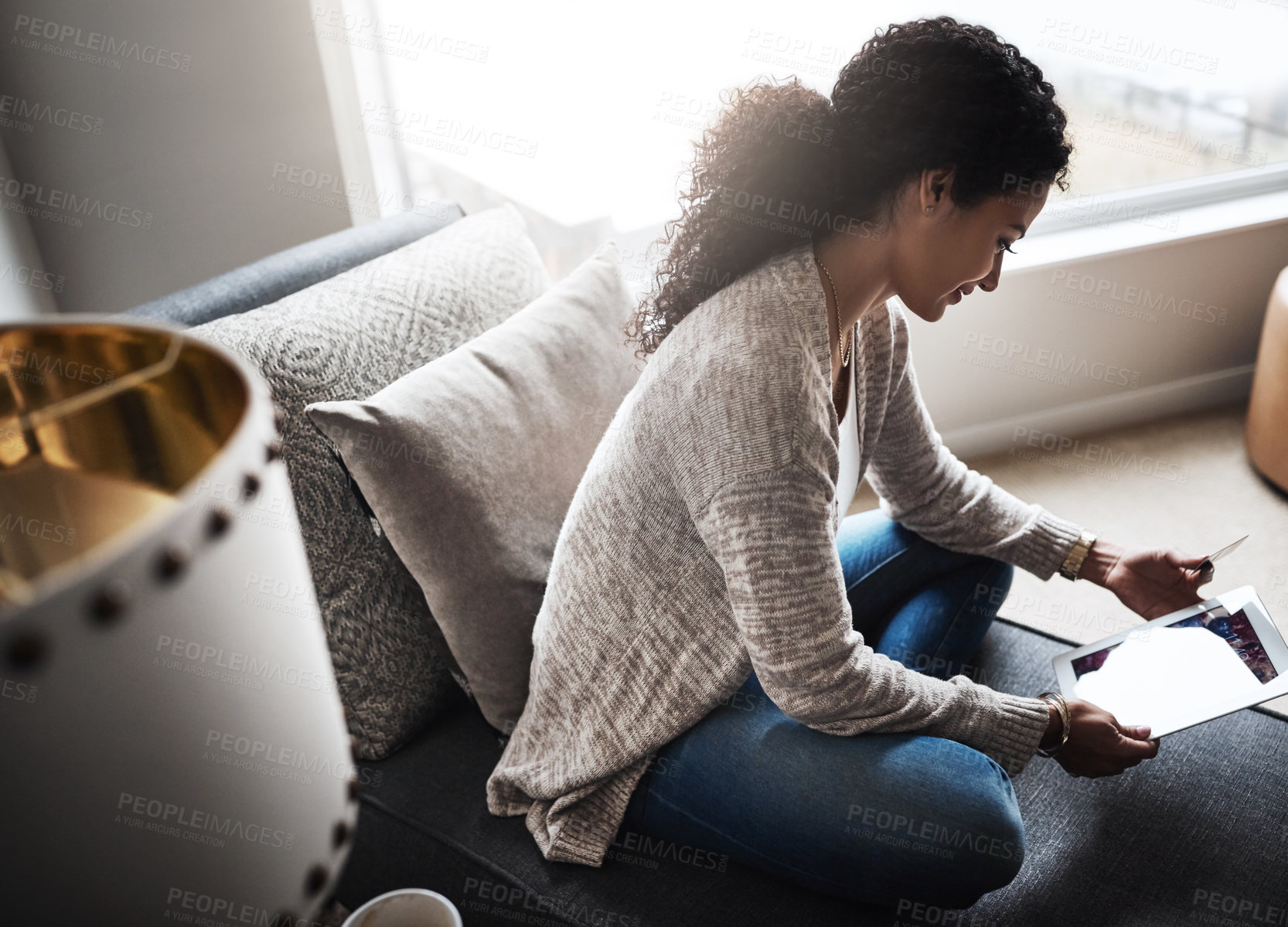 Buy stock photo Shot of a cheerful young woman relaxing on a chair while  doing online shopping on a digital tablet at home