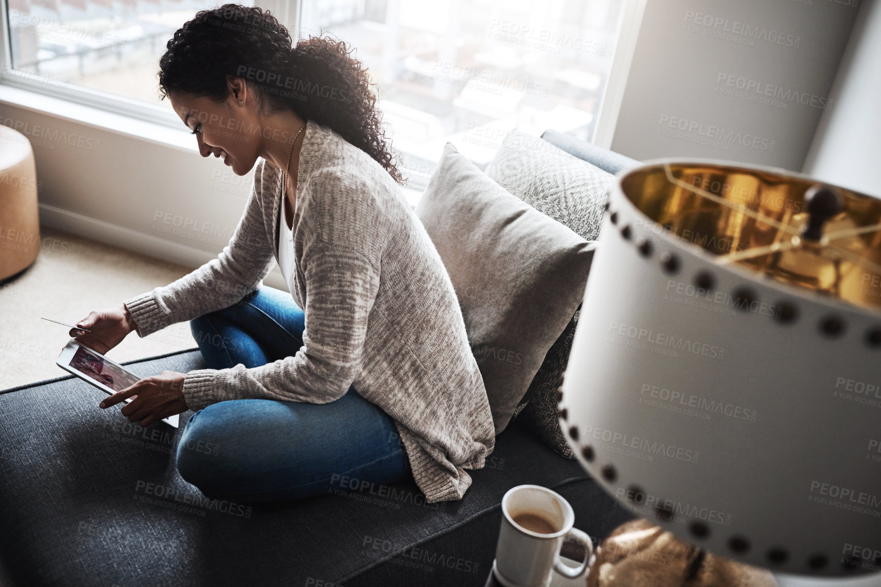 Buy stock photo Shot of a cheerful young woman relaxing on a chair while  doing online shopping on a digital tablet at home