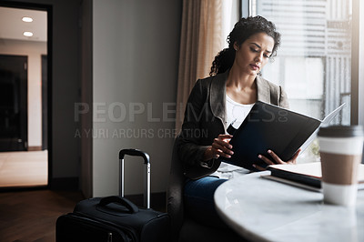 Buy stock photo Shot of a young businesswoman reading through a business folder while waiting for her flight in an airport lounge