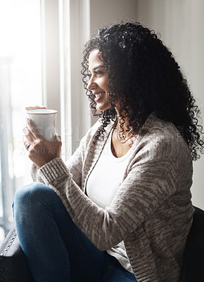 Buy stock photo Shot of a cheerful young woman enjoying a cup of coffee while being seated on a chair at home during the day