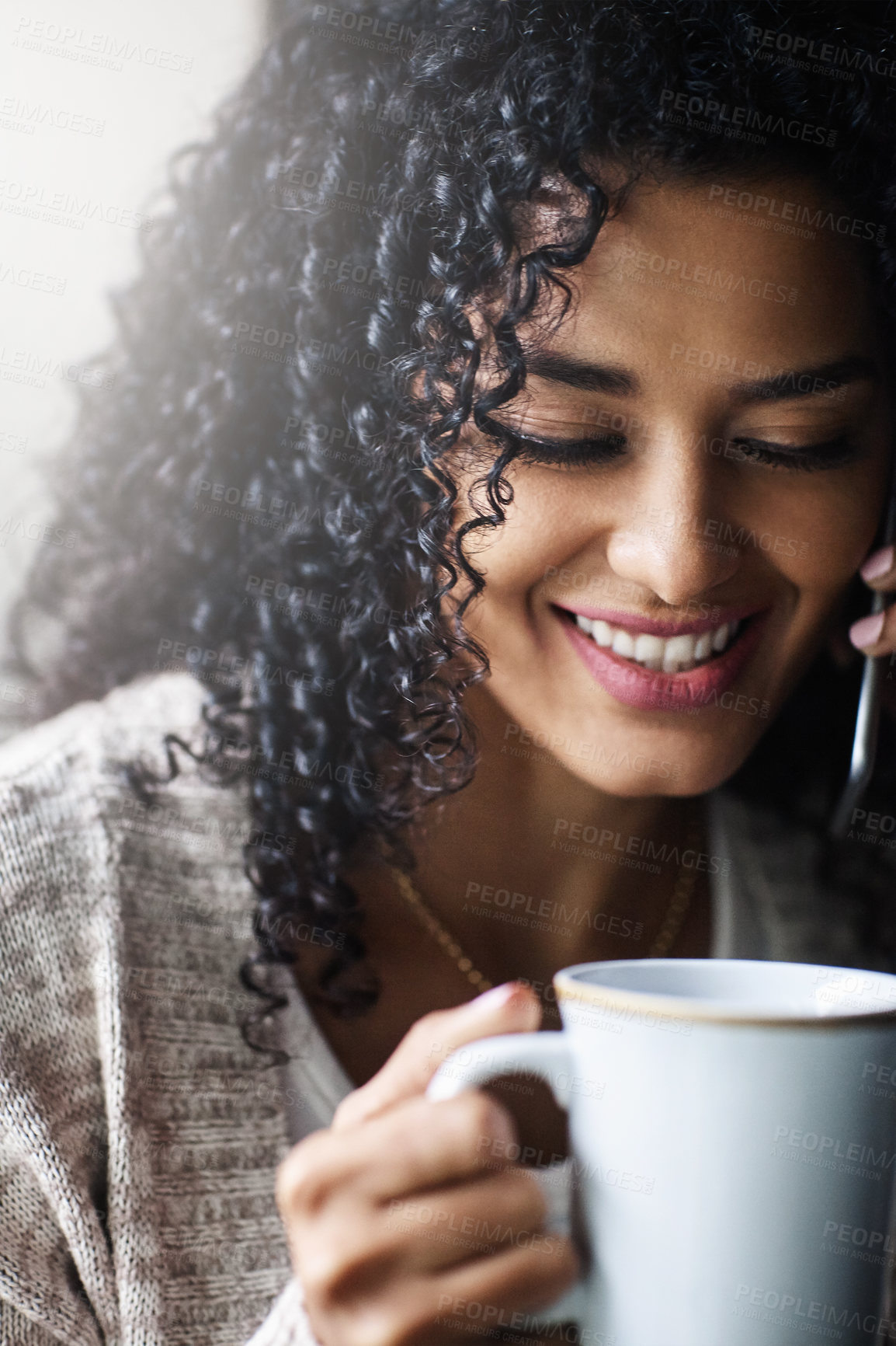 Buy stock photo Shot of a cheerful young woman relaxing and drinking coffee while talking on her cellphone at home during the day