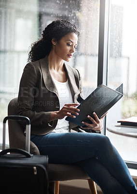 Buy stock photo Shot of a young businesswoman reading through a business folder while waiting for her flight in an airport lounge