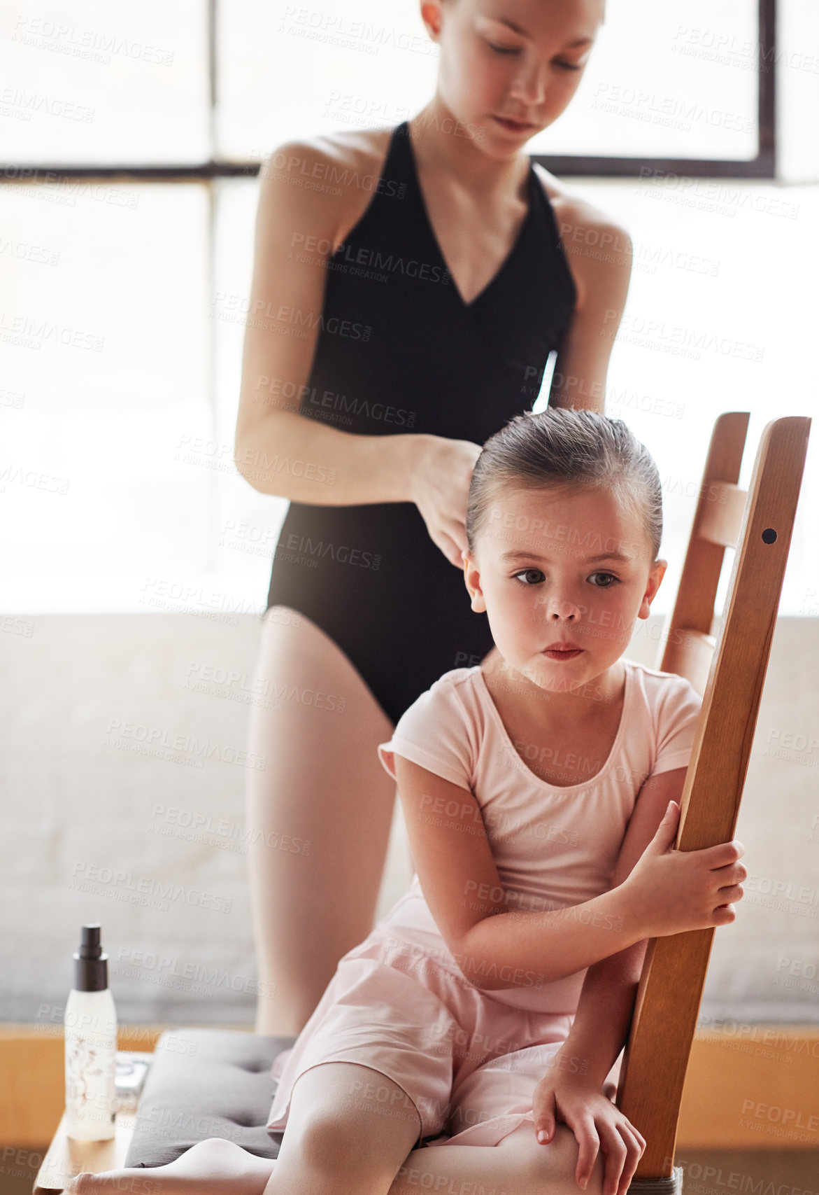 Buy stock photo Shot of an adorable little girl getting her hair tied up by an older girl in a ballet studio