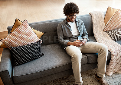 Buy stock photo Shot of a handsome young man using his cellphone while relaxing on the couch at home