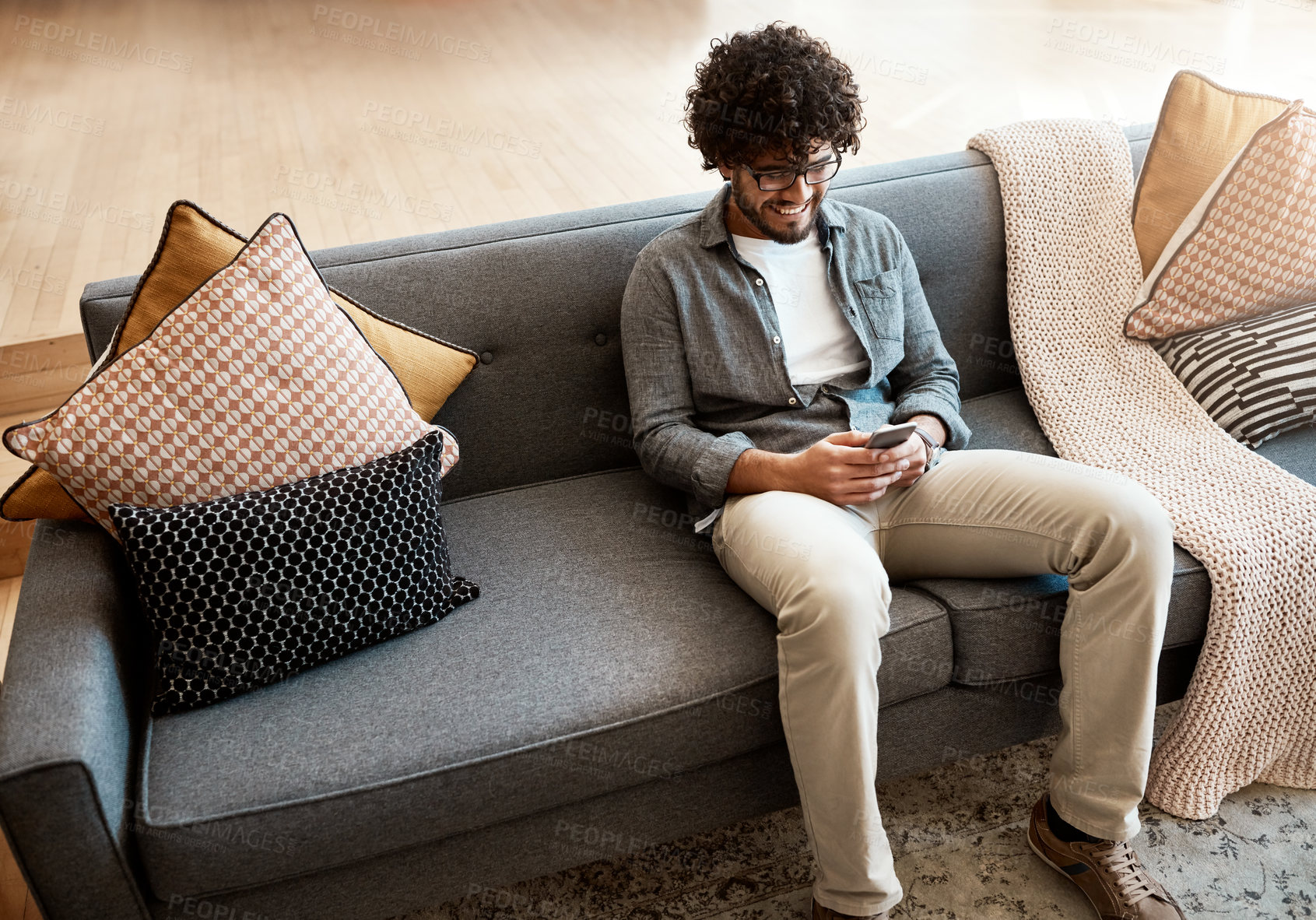 Buy stock photo Shot of a handsome young man using his cellphone while relaxing on the couch at home