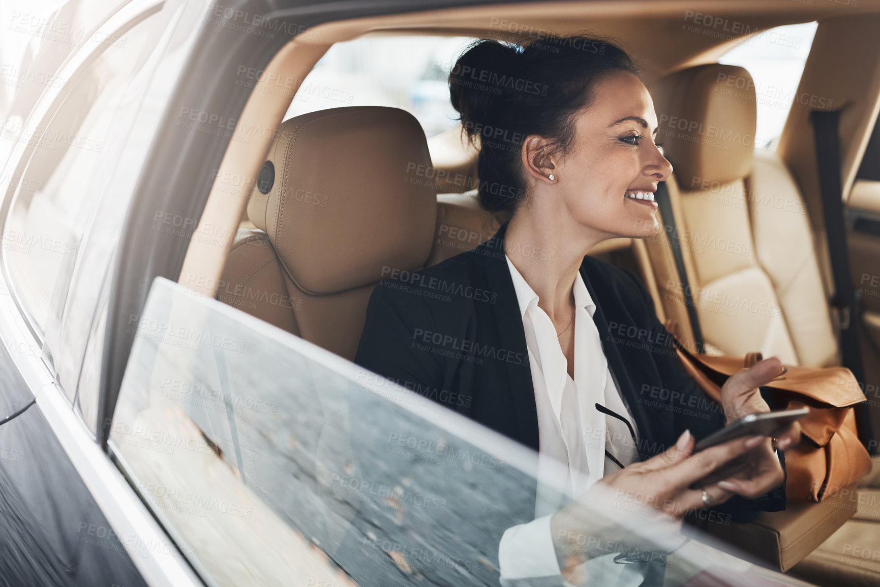 Buy stock photo Shot of a cheerful young businesswoman seated in a car as a passenger while texting on her phone on her way to work