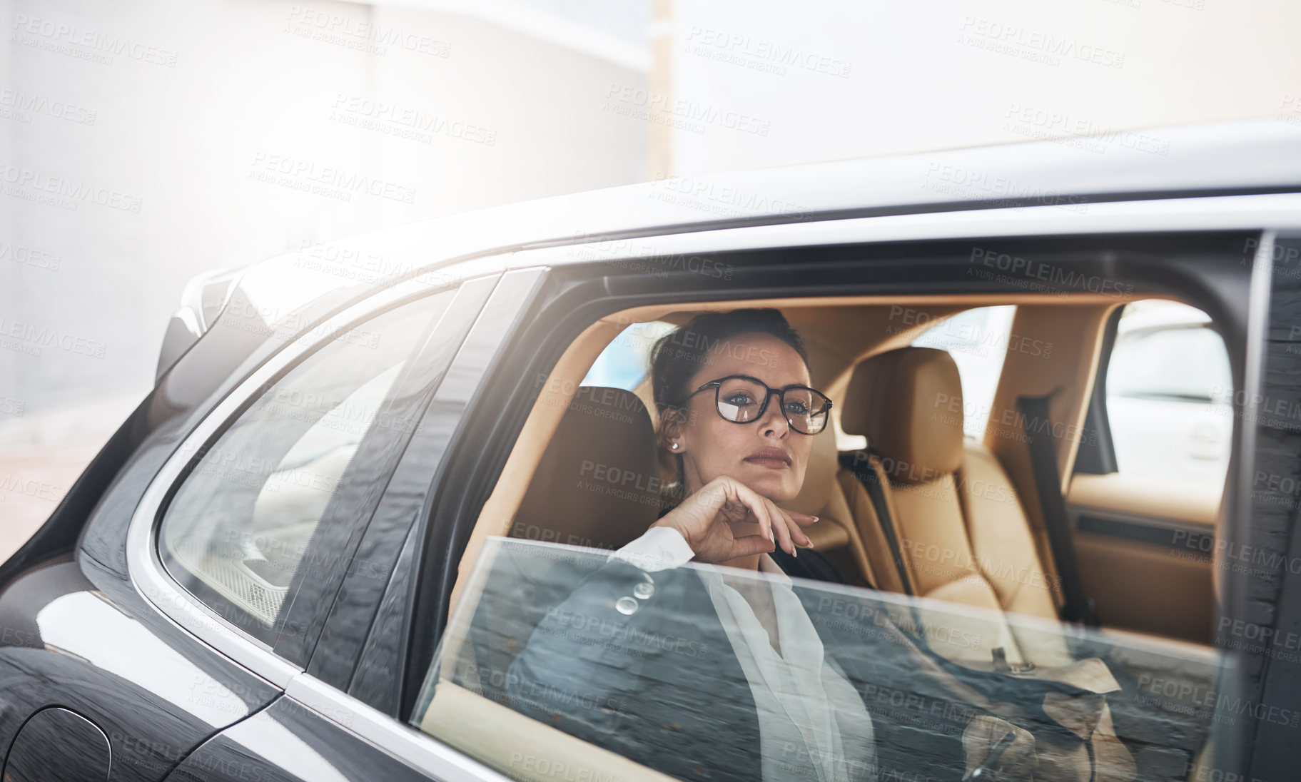 Buy stock photo Shot of a confident young businesswoman seated in a car as a passenger while looking out the window on her way to work