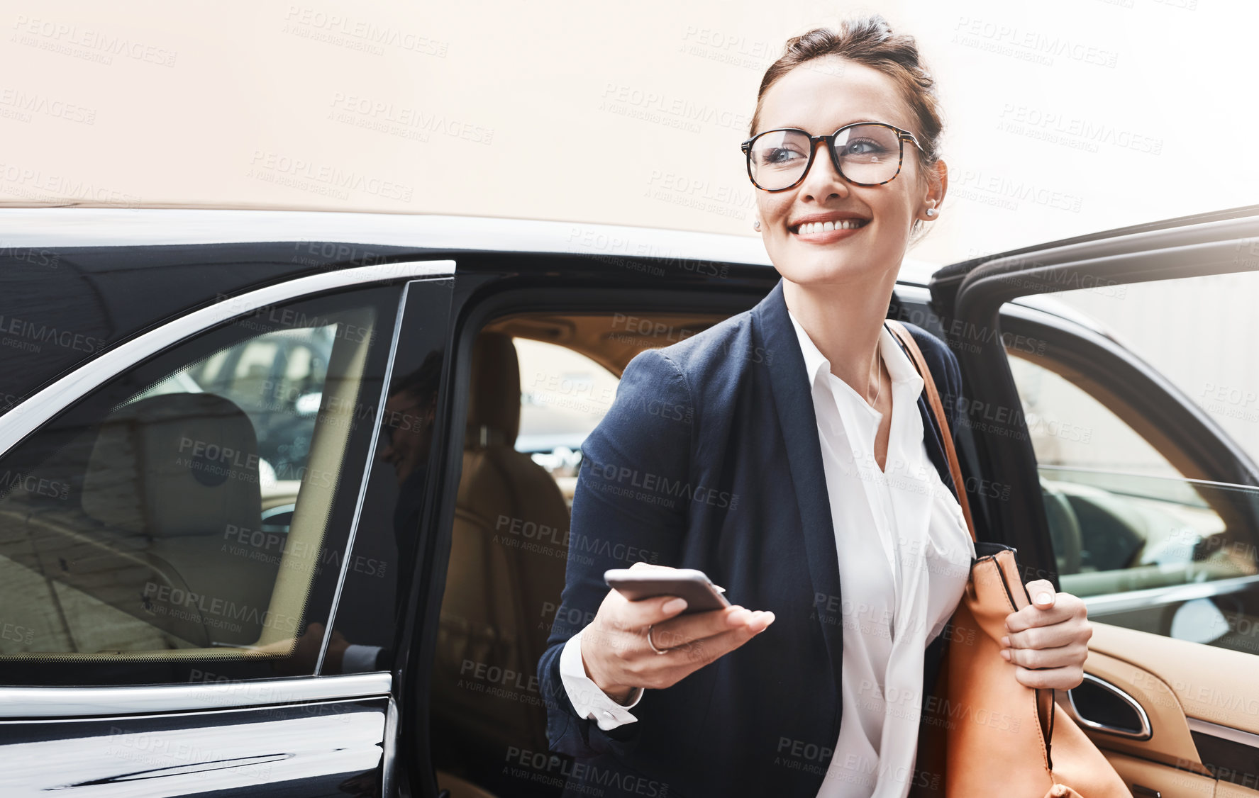 Buy stock photo Shot of a cheerful young businesswoman getting out of a car while holding a cellphone outside during the day