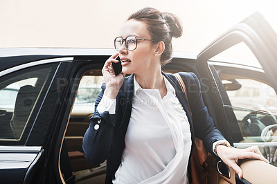 Buy stock photo Shot of a confident young businesswoman getting out of a car while holding a cellphone outside during the day