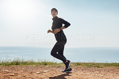Buy stock photo Shot of a determined young woman going for a jog on her own with a view of the ocean in the background