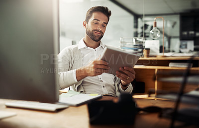 Buy stock photo Shot of a handsome young businessman using a digital tablet while working late in an office