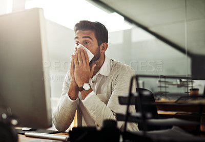 Buy stock photo Shot of a handsome young businessman blowing his nose while working late in an office