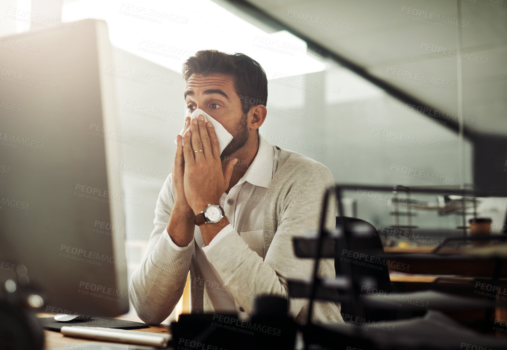 Buy stock photo Shot of a handsome young businessman blowing his nose while working late in an office