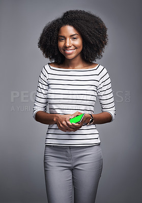 Buy stock photo Studio portrait of a young woman holding a mobile phone against a gray background