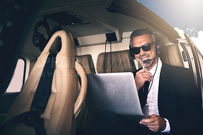 Buy stock photo Shot of a mature businessman using a laptop while traveling in a helicopter