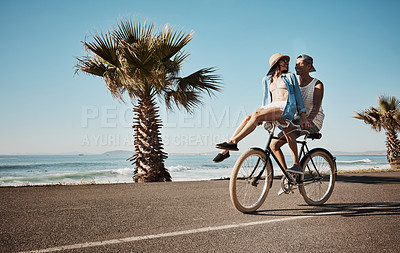 Buy stock photo Shot of a young couple riding a bicycle together on the promenade