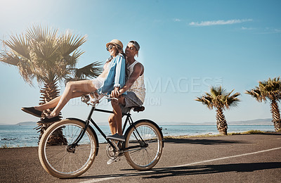 Buy stock photo Shot of a young couple riding a bicycle together on the promenade