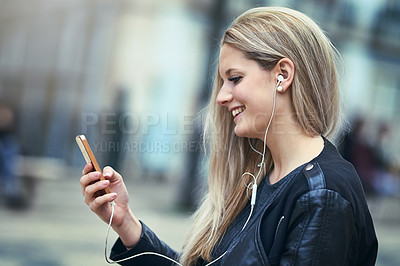 Buy stock photo Shot of an attractive woman using a mobile phone and earphones in the city