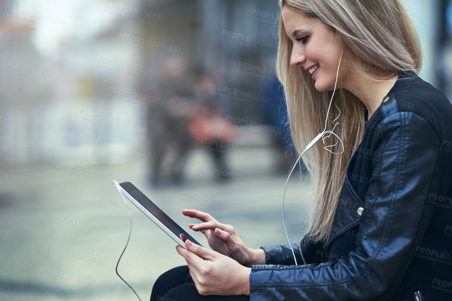 Buy stock photo Shot of an attractive woman using a digital tablet and earphones in the city