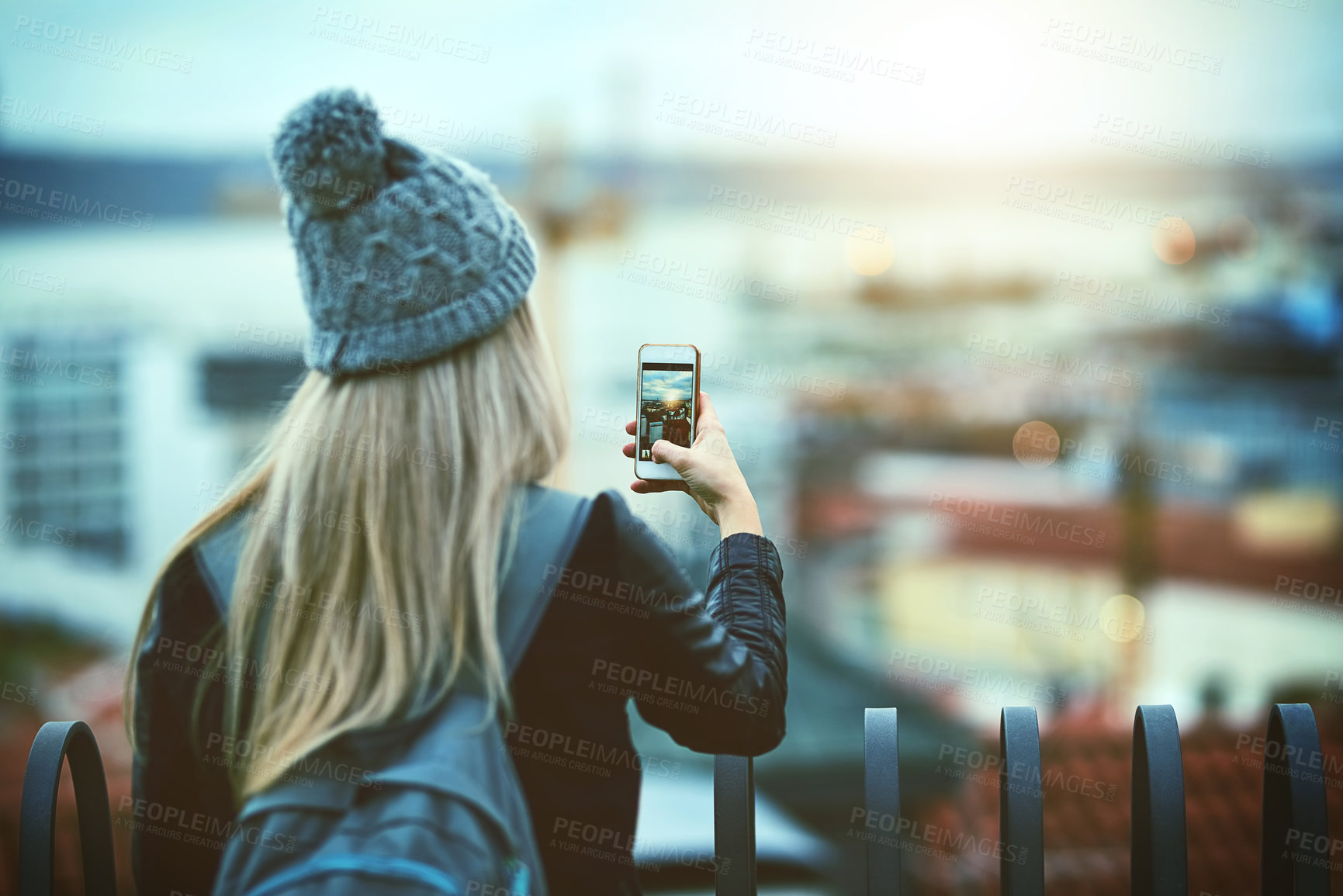 Buy stock photo Rearview shot of a young woman using a cellphone to take pictures of a city view from a bridge