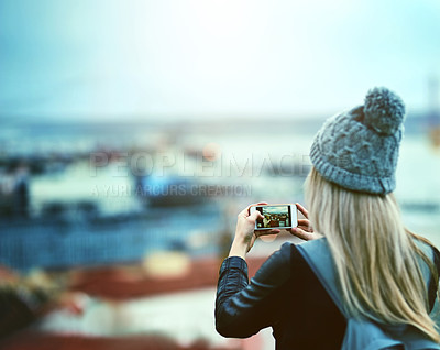 Buy stock photo Rearview shot of a young woman using a cellphone to take pictures of a city view
