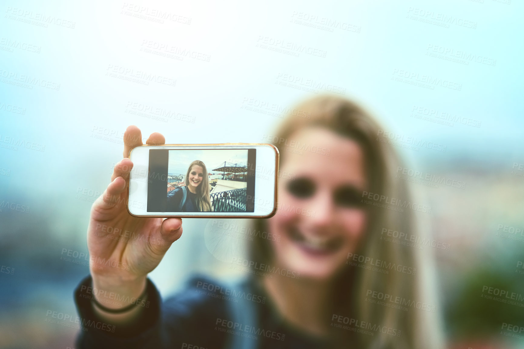 Buy stock photo Shot of a young woman using a cellphone to take selfies in the city