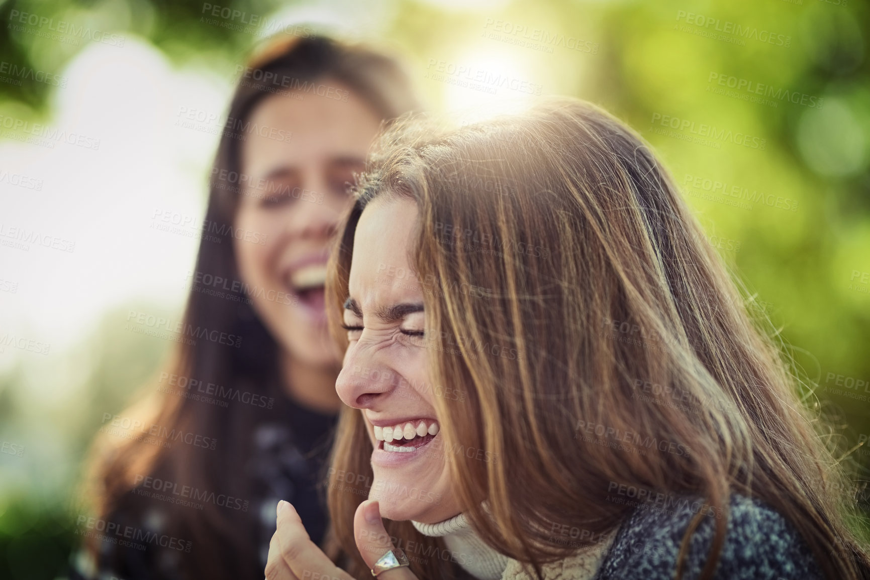 Buy stock photo Cropped shot of two attractive young women laughing while sitting in the park