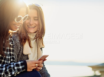 Buy stock photo Friends, happy and women in nature with phone for social media, internet and online chatting outdoors. Beach, smile and people on smartphone for dating website on weekend, holiday and relax on bench