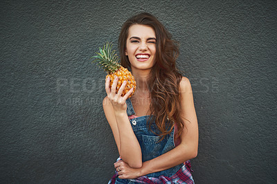 Buy stock photo Portrait of a cheerful young woman holding a pineapple while winking and standing against a grey background