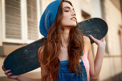 Buy stock photo Shot of an attractive young female skater holding a skateboard behind her back outside during the day