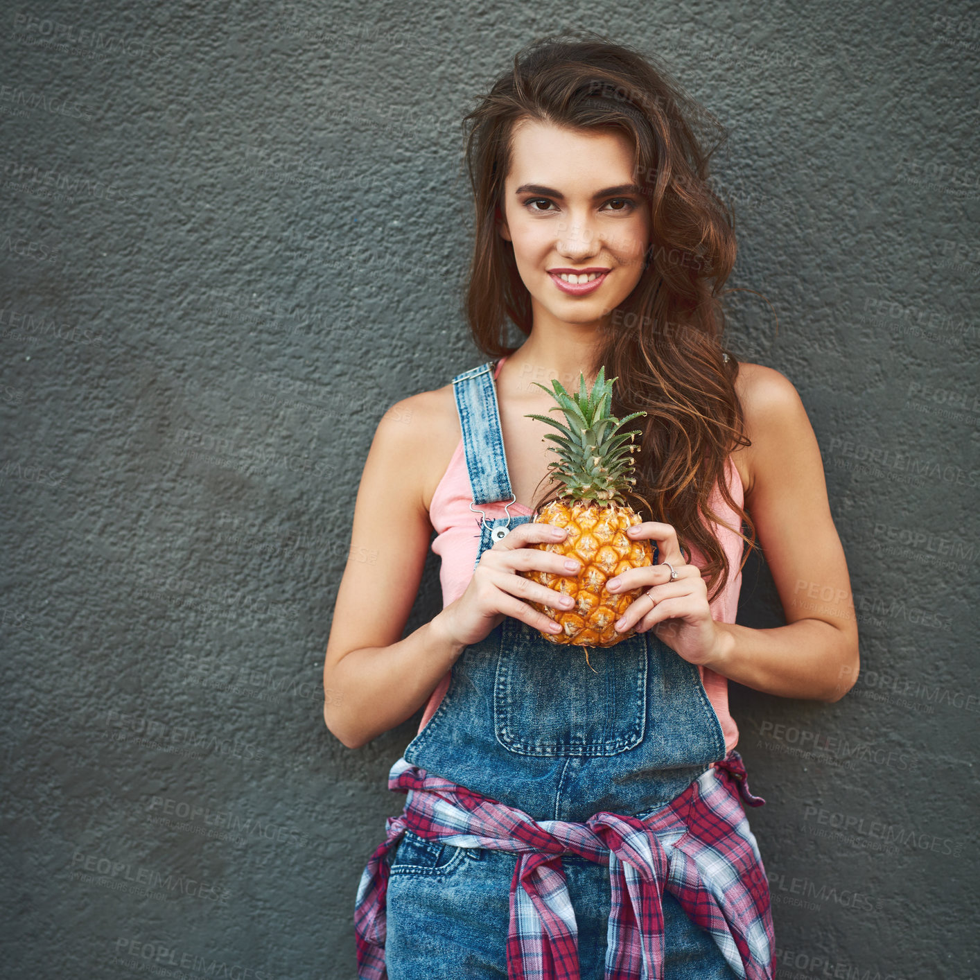 Buy stock photo Portrait of a cheerful young woman holding a pineapple while standing against a grey background