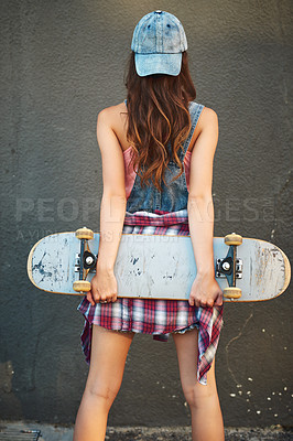 Buy stock photo Rearview shot of an unrecognizable young woman standing with a skateboard behind her back against a grey background