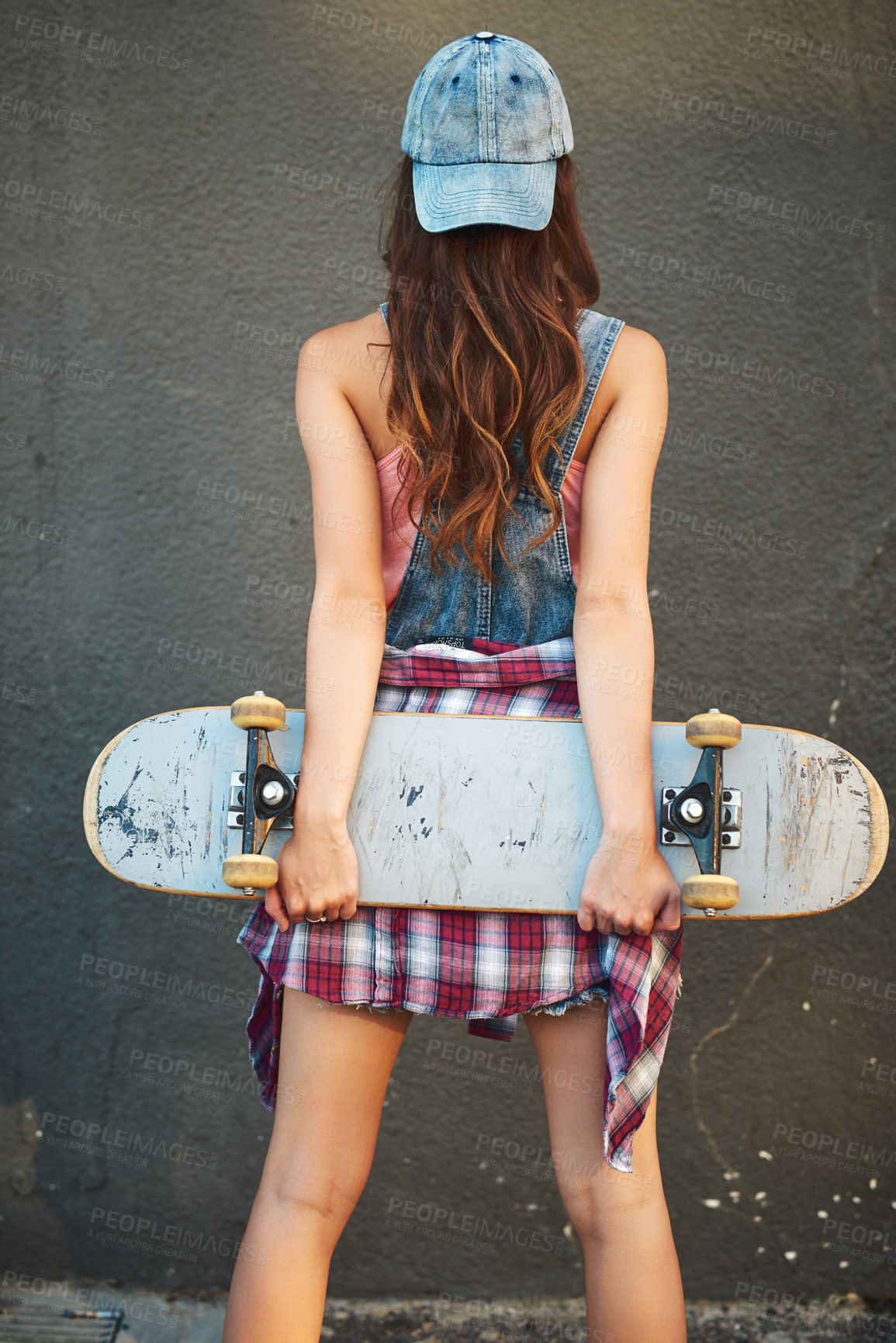 Buy stock photo Rearview shot of an unrecognizable young woman standing with a skateboard behind her back against a grey background