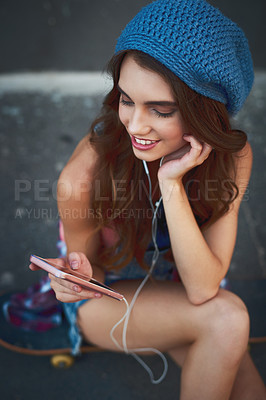 Buy stock photo Shot of a carefree young woman seated on the floor while listening to music through her earphones outside during the day