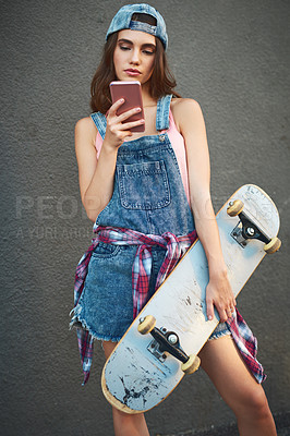 Buy stock photo Shot of an attractive young woman holding a skateboard while texting on her cellphone against a grey background