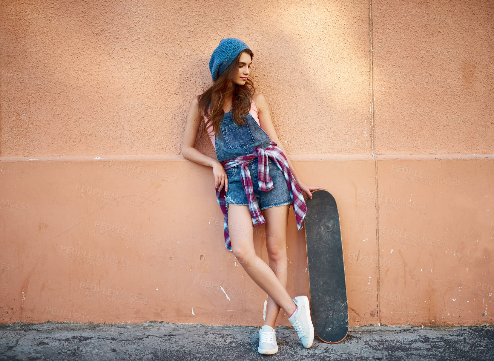 Buy stock photo Shot of a carefree young woman standing with her skateboard against a orange background