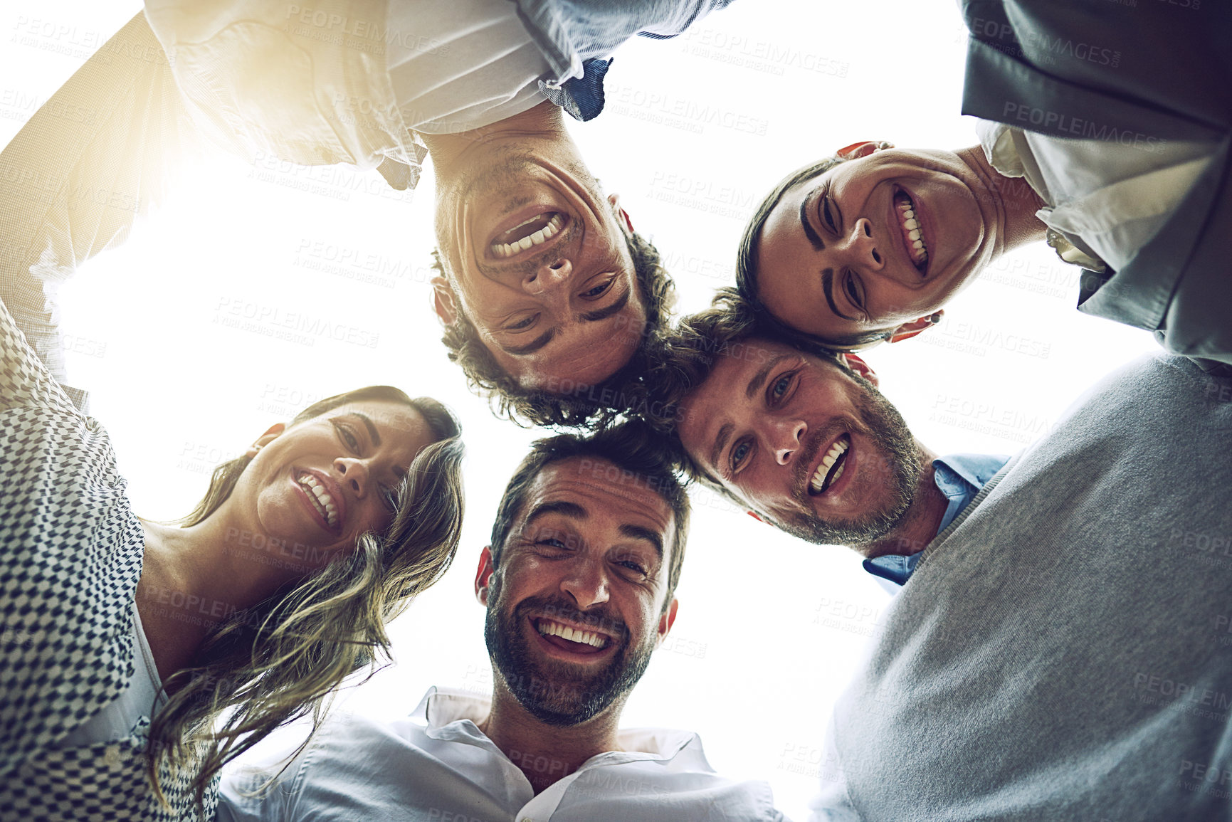 Buy stock photo Low angle portrait of a group of cheerful young work colleagues standing in a circle and looking down outside during the day